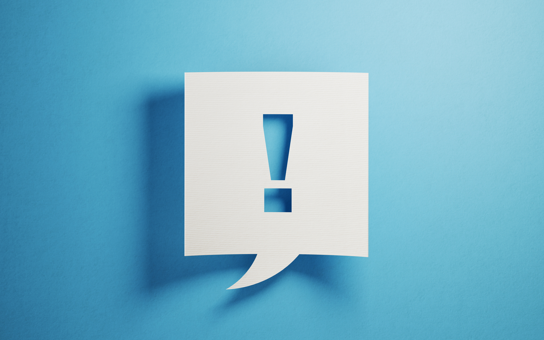 White chat bubble on blue background. There is an exclamation point on chat bubble. Horizontal composition with copy space.