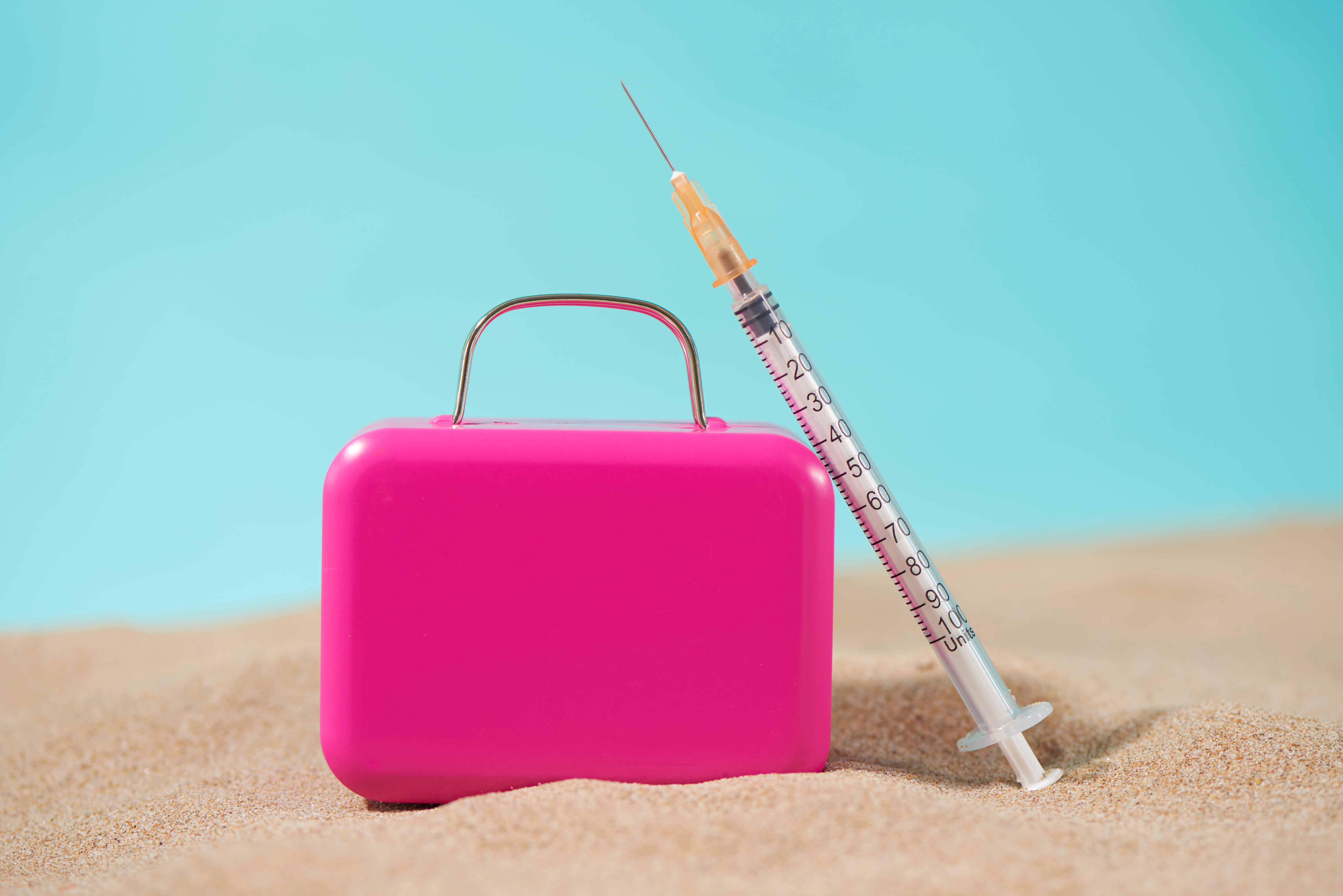 A,Syringe,And,A,Pink,Suitcase,On,The,Sand,,On