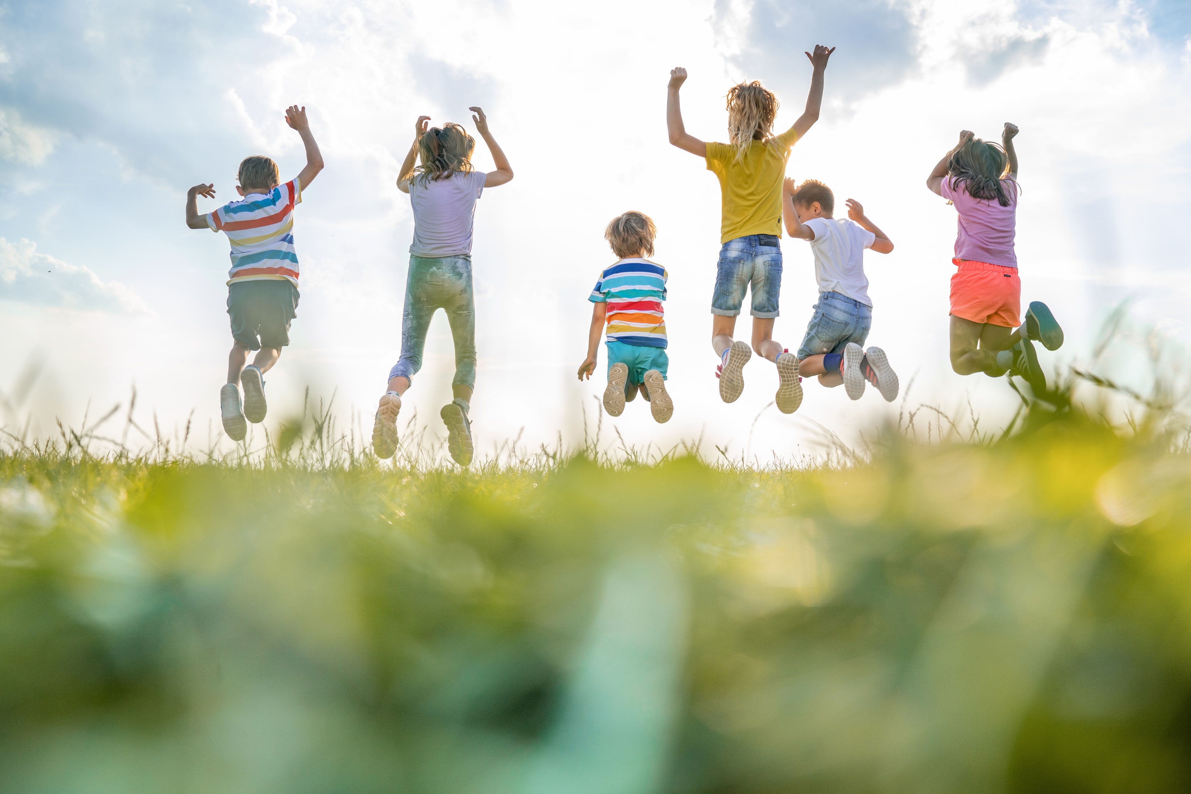 Fröhliche Kinder mit erhobenen Armen springen in der Natur. Rückansicht.