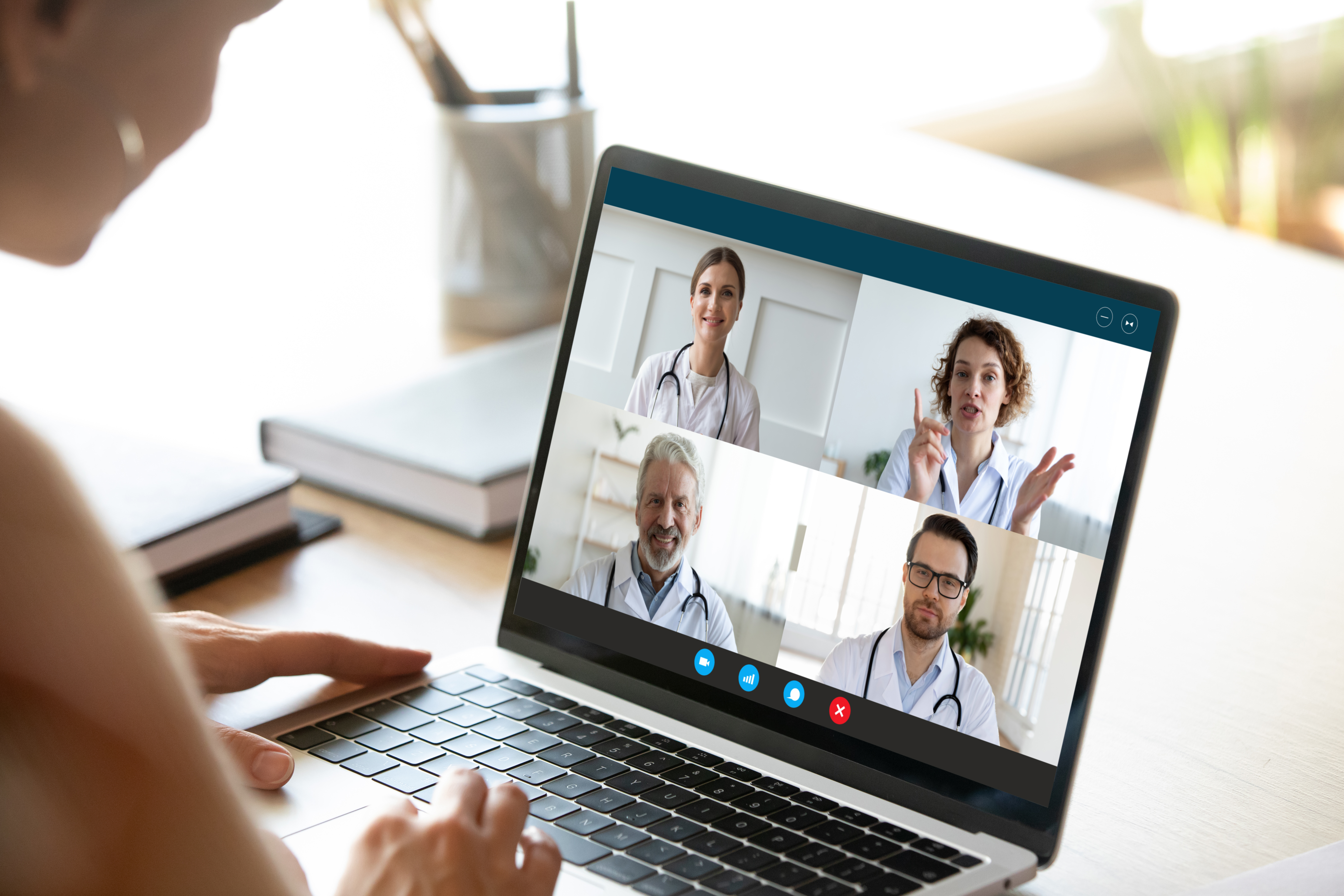Seitenansicht eines Laptops, auf dem gerade zwei Ärztinnen und zwei Ärzte in einem virtuellen Call miteinander sprechen.