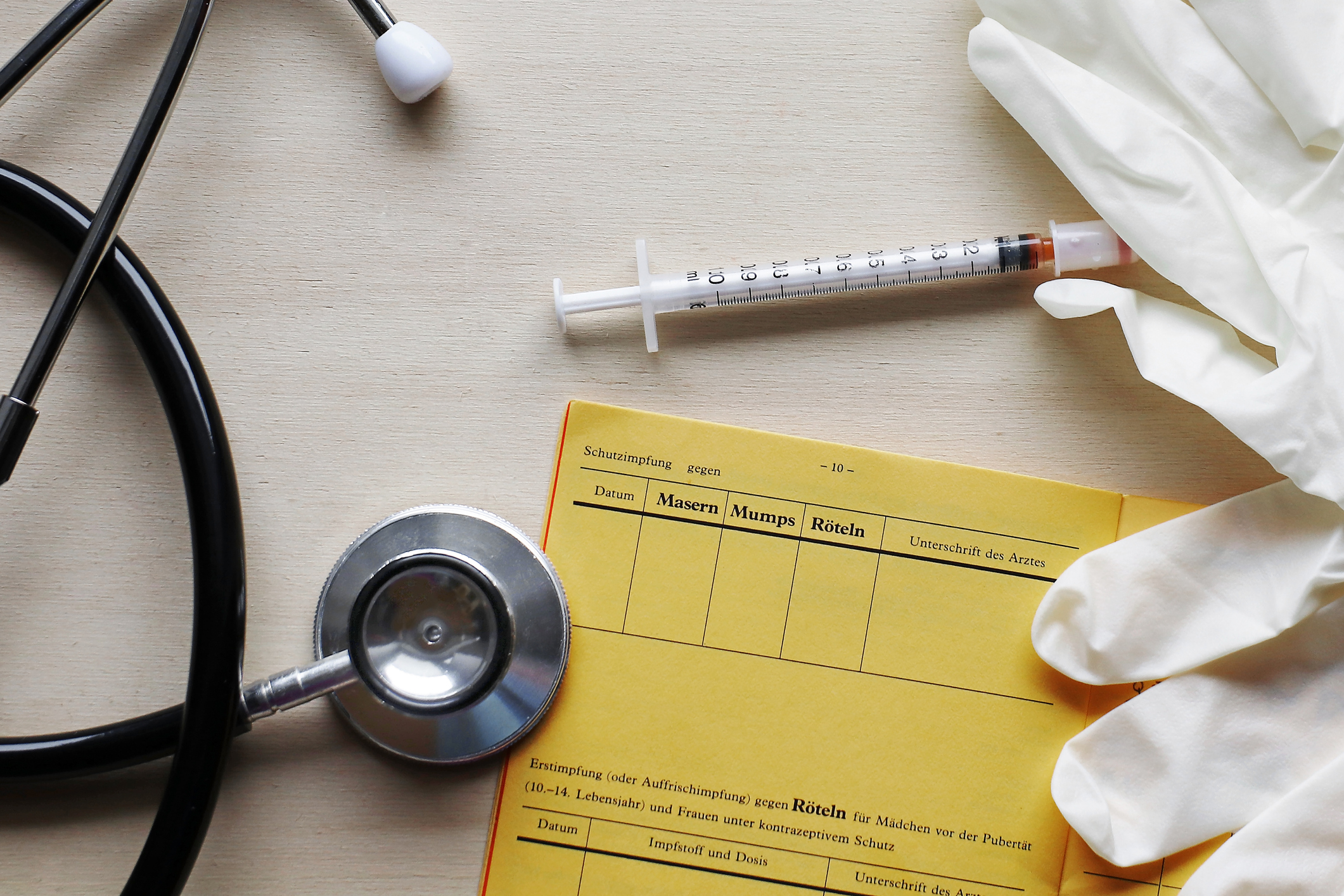 Ein Stethoskop, ein Impfausweis und eine Spritze liegen auf einem Tisch