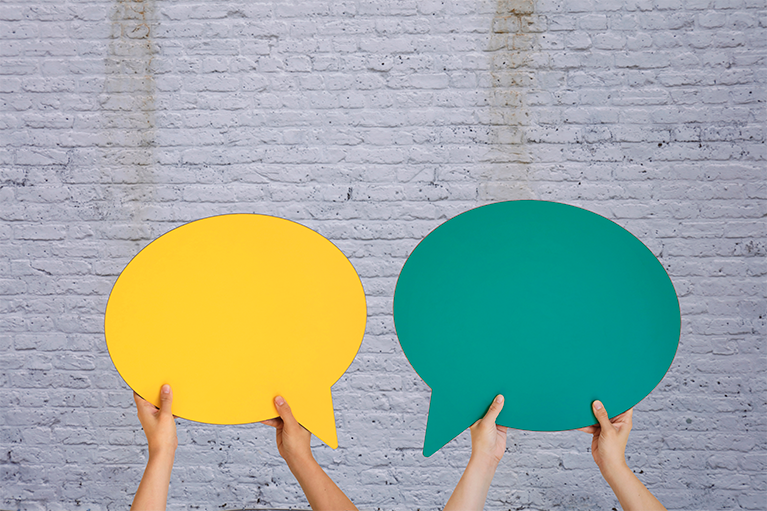 Eine gelbe und eine grüne Sprechblase, gehalten von Händen.