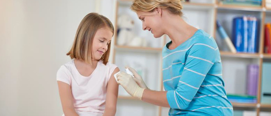 Eine medizinische Fachangestellte desinfiziert den Oberarm eines Mädchens.