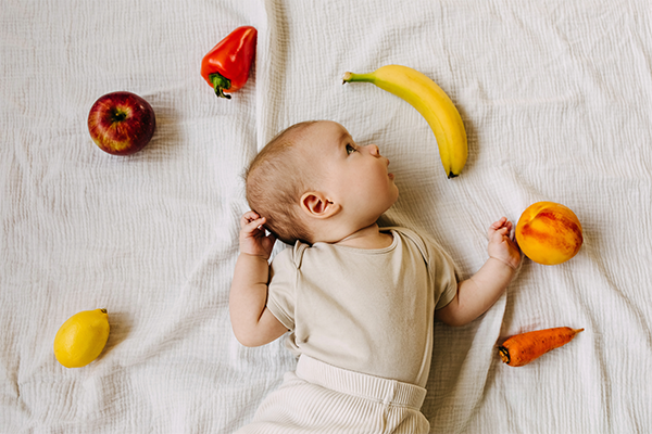 Baby liegt auf einer Decke umgeben von Obst.