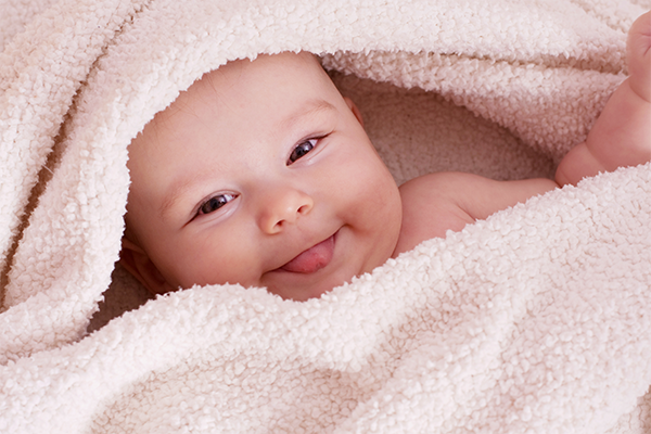Baby liegt eingekuschelt in einer Decke und lacht in die Kamera.