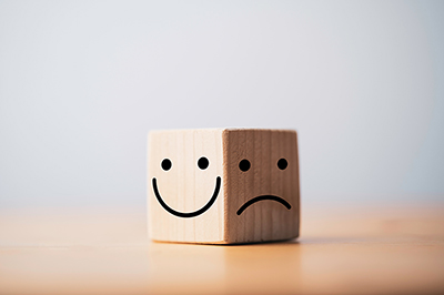 Ein glücklicher Smiley und ein trauriger Smiley auf einem Würfel.