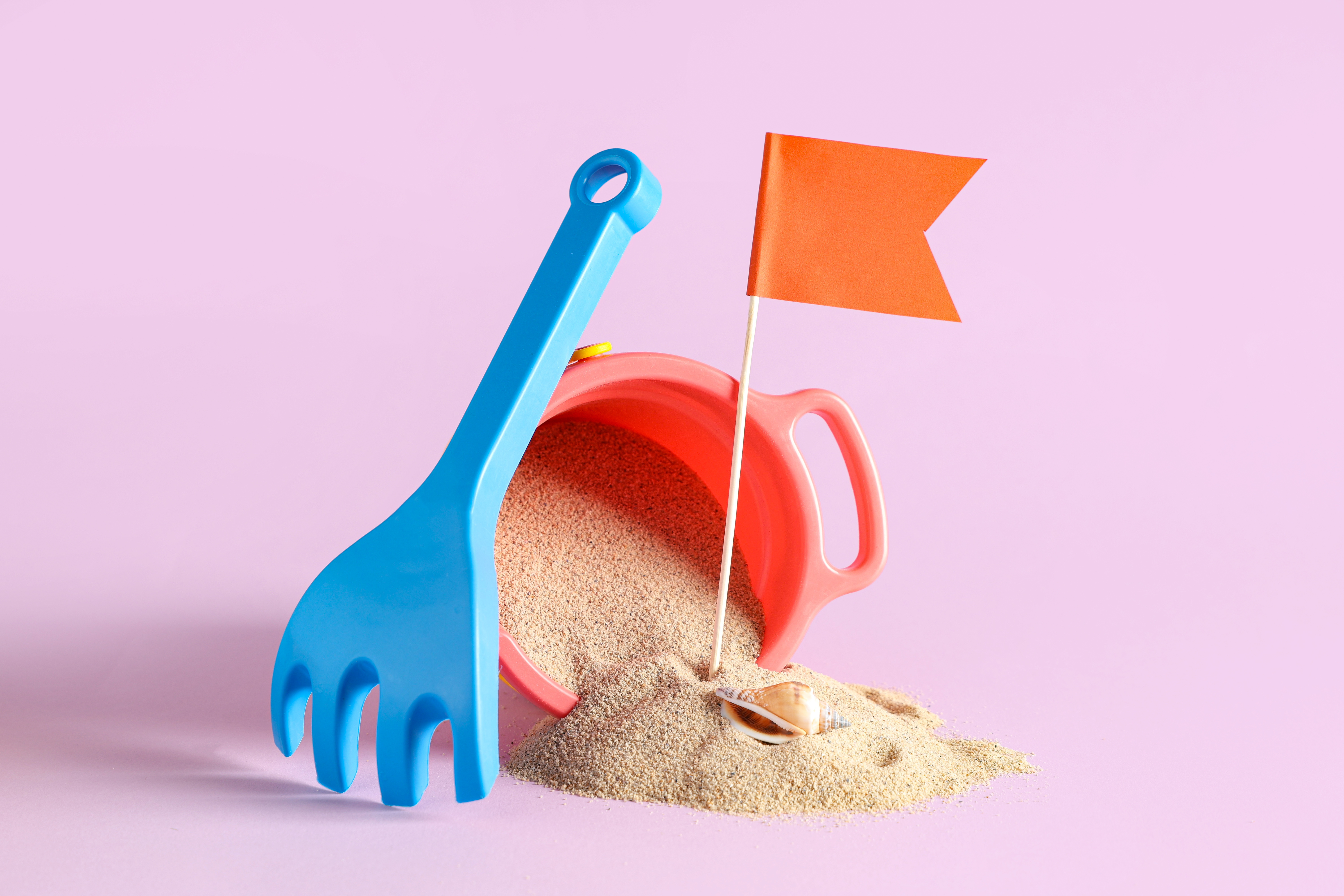 Eimer, Harke und Sand, in dem ein rotes Fähnchen steckt.