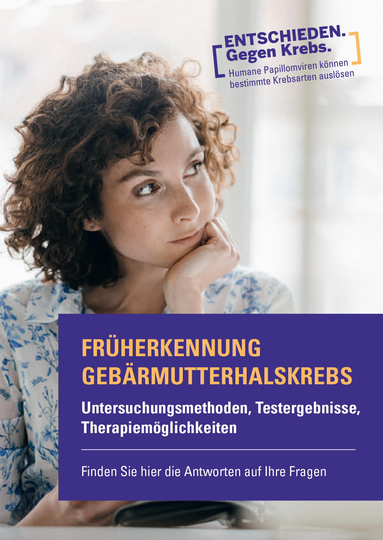 Eine nachdenklich wirkende junge Frau mit lockigem braunem Haar sitzt an einem Schreibtisch in einem hellen Raum. Sie trägt eine blumig gemusterte Bluse und hält ein Smartphone in der Hand, während sie aus dem Fenster blickt.