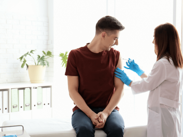 Das Bild zeigt einen jungen Mann und medizinisches Fachpersonal bei einer Impfung.