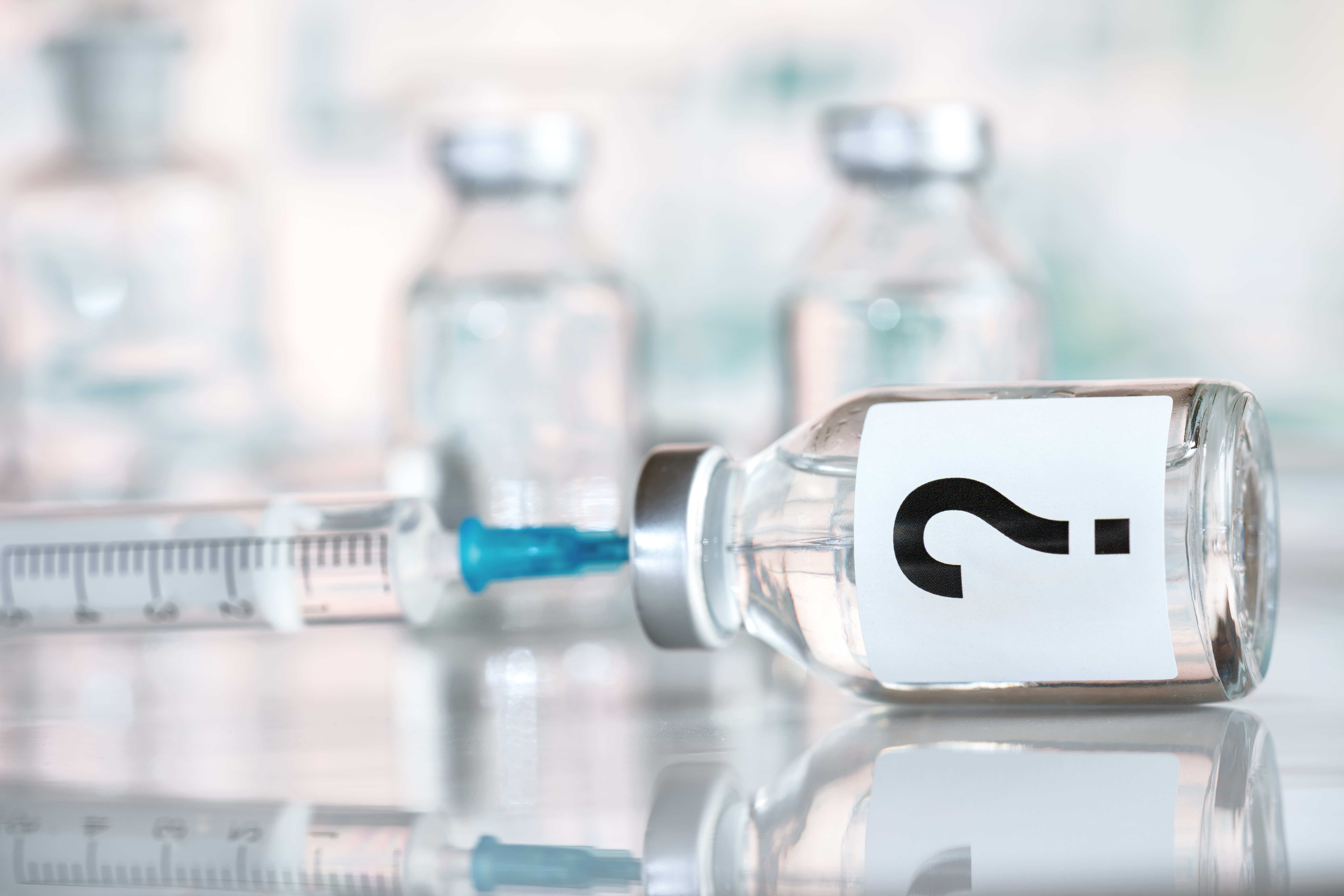 Spritze, mit der Impfstoff aufgezogen wird, Impfstoff ist mit einem großen Fragezeichen beschriftet