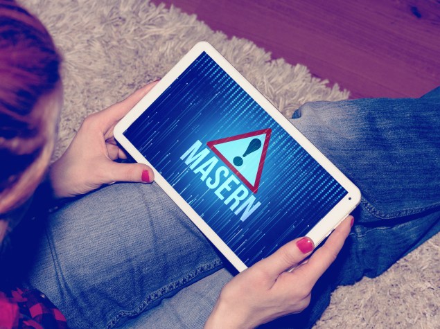 Frau hält ein Tablet in den Händen und bildet ein rotes Dreieck mit Ausrufezeichen ab und darunter steht Masern
